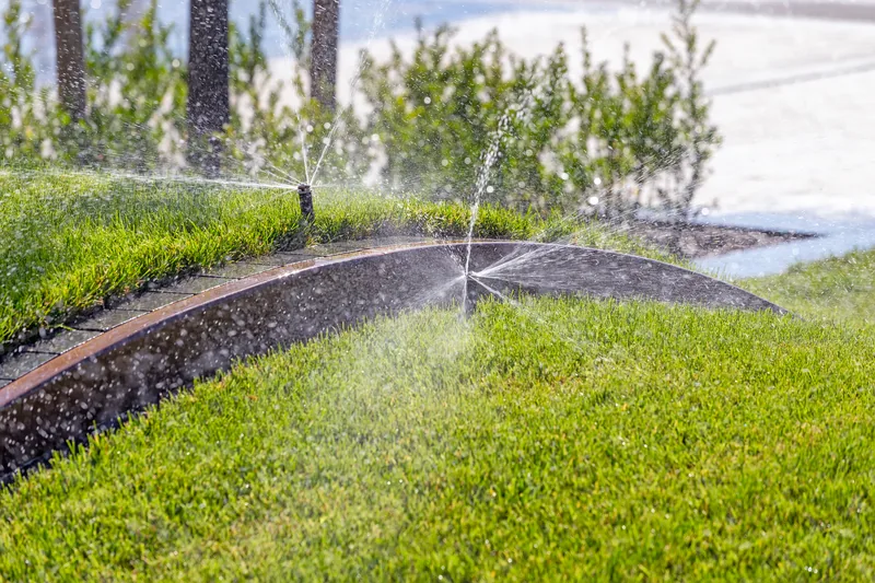 Two pop-up heads watering turf either side of a curved paver walkway